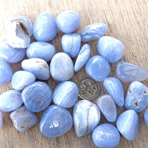 May include: A collection of blue lace agate tumbled stones. The stones are smooth and polished, with a variety of blue and white patterns.