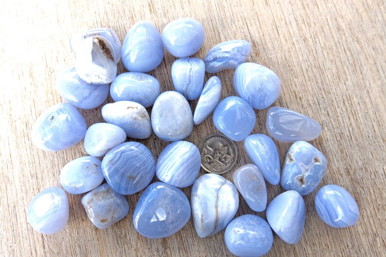 May include: A collection of blue lace agate tumbled stones. The stones are smooth and polished, with a variety of blue and white patterns.
