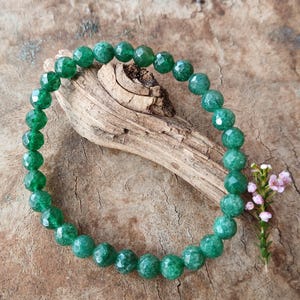 May include: A circular bracelet composed of faceted, translucent emerald green beads. The beads are strung together in a continuous loop, displaying a consistent round shape and a reflective, polished surface texture throughout the entire piece.