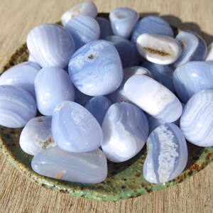 May include: A collection of blue agate tumbled stones in a green ceramic dish. The stones are smooth and polished, with a variety of blue and white patterns.