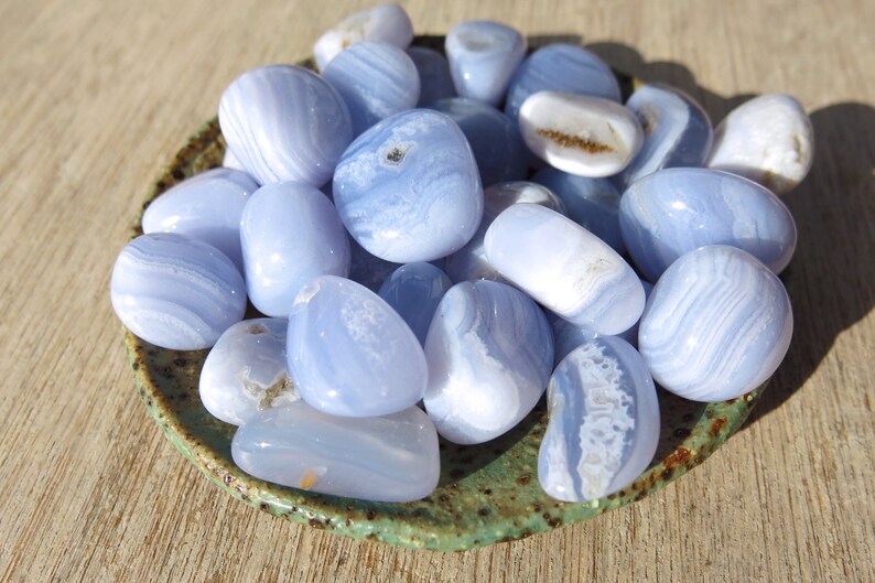 May include: A collection of blue agate tumbled stones in a green ceramic dish. The stones are smooth and polished, with a variety of blue and white patterns.