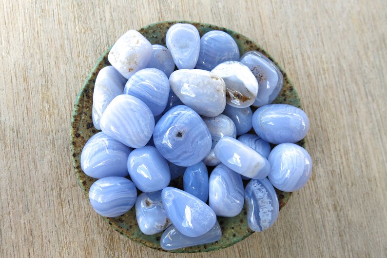 May include: A bowl filled with blue agate tumbled stones. The stones are smooth and polished, with a variety of blue and white patterns.