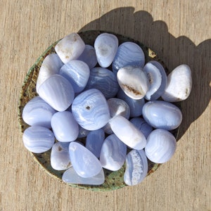 May include: A bowl filled with blue agate tumbled stones. The stones are smooth and polished, with a variety of blue and white patterns.