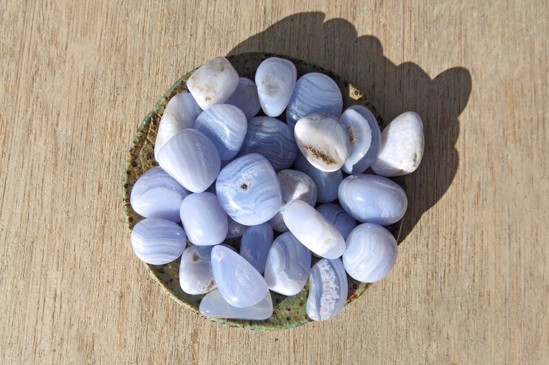 May include: A bowl filled with blue agate tumbled stones. The stones are smooth and polished, with a variety of blue and white patterns.