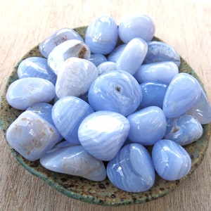 May include: A collection of blue agate tumbled stones in a small ceramic dish. The stones are smooth and polished, with a variety of blue and white patterns.