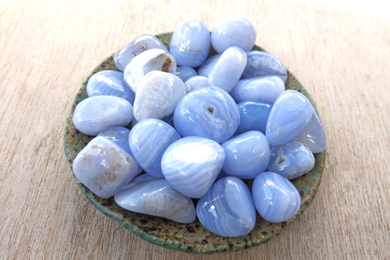 May include: A collection of blue agate tumbled stones in a small ceramic dish. The stones are smooth and polished, with a variety of blue and white patterns.