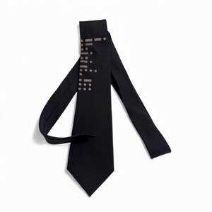 May include: A black necktie with a geometric pattern of small, light-colored dots and dashes. The tie is made of a smooth, dark fabric and is displayed against a white background. The tie is a classic accessory.