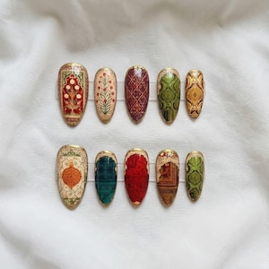 Peut inclure: Dix faux ongles ovales ornés de motifs complexes. Les ongles présentent des motifs rouges, verts, dorés et crème, avec des bordures dorées. Les motifs comprennent des motifs floraux, géométriques et des textures de type tapis, offrant un look unique et artistique.