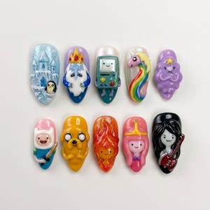 May include: A set of ten 3D press-on nails featuring colorful character designs from Adventure Time, including an ice castle, Ice King, BMO, Lady Rainicorn, Lumpy Space Princess, Finn, Jake, Flame Princess, Princess Bubblegum, and Marceline.