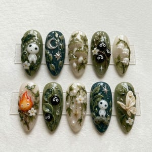 May include: A set of ten press-on nails featuring intricate 3D designs inspired by forest themes. The nails display motifs including a white forest spirit, a silver crescent moon, mushrooms, soot sprites, lily of the valley, a flame, and a moth.