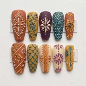 May include: A collection of ten press-on nails with detailed, raised patterns. The nails display a range of colours, such as orange, yellow, teal, and purple, with floral and geometric designs. Each nail is mounted on a clear plastic strip.
