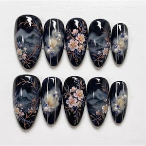 May include: A set of ten black artificial nails with a glossy finish. Each nail features a hand-painted design of a mountain landscape, delicate pink flowers, and pearl accents. The nails are oval-shaped and arranged on a white surface.