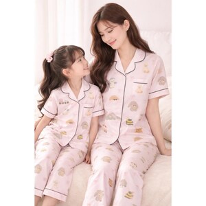 Puede incluir: Conjuntos de pijama rosa a juego con un estampado de animales caprichoso. Los conjuntos incluyen camisas de manga corta con botones y pantalones, ribeteados con ribetes negros. Una madre y su hijo llevan los pijamas, sonri&eacute;ndose.