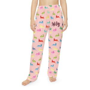 Puede incluir: Pantalones de pijama rosas con un estampado de conejos coloridos. Los conejos son de varios colores, incluyendo rojo, azul, verde y amarillo. El nombre "Mily" est&aacute; escrito en cursiva en los pantalones.