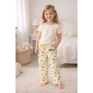 Puede incluir: Una ni&ntilde;a peque&ntilde;a con un pijama amarillo claro. La parte superior tiene un gr&aacute;fico de conejito amarillo y ribete. Los pantalones del pijama son de color amarillo claro con ilustraciones de conejitos coloridos y el nombre "Emily" en escritura.