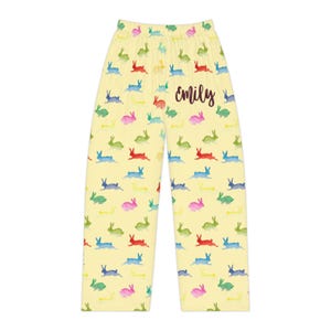 Puede incluir: Pantalones de pijama amarillos claros con un patr&oacute;n repetido de conejos coloridos en verde, azul, rojo y rosa. El nombre "emily" est&aacute; escrito en cursiva en los pantalones.