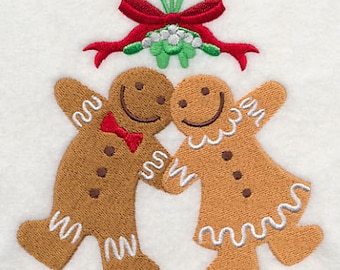 May include: Two gingerbread people stand under a sprig of mistletoe with a red bow. They are smiling and holding hands.
