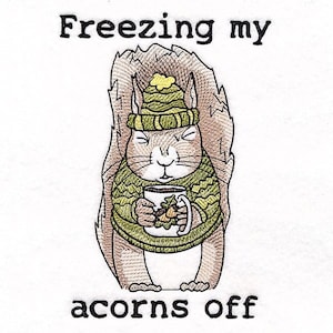 May include: A cartoon squirrel wearing a green and yellow hat and a green sweater is holding a mug of hot chocolate. The text "Freezing my acorns off" is written above and below the squirrel.