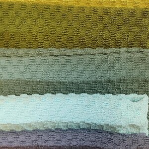 May include: A vertical image showcasing a collection of textured, colorful towels. The towels are arranged in horizontal stripes of varying shades, including cream, orange, yellow, green, blue, and brown. The towels have a waffle-like weave.