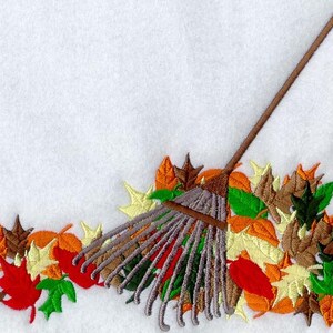 May include: A brown rake with gray tines is surrounded by a pile of colorful fall leaves. The leaves are red, orange, yellow, and green. The rake is lying on a white background.
