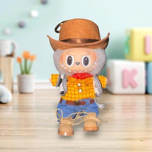 May include: A plush toy cowboy doll with a brown hat, yellow plaid shirt, blue jeans, and tan boots. The doll has a white face with large eyes and a red neckerchief. The doll is standing on a wooden surface.