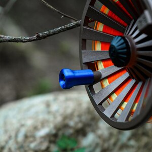 K&ouml;nnte beinhalten: Nahaufnahme einer Fliegenfischrolle mit braunem Rahmen und blauem Griff. Die Rolle hat orangefarbene und gelbe Angelschnur. Der Hintergrund ist unscharf.