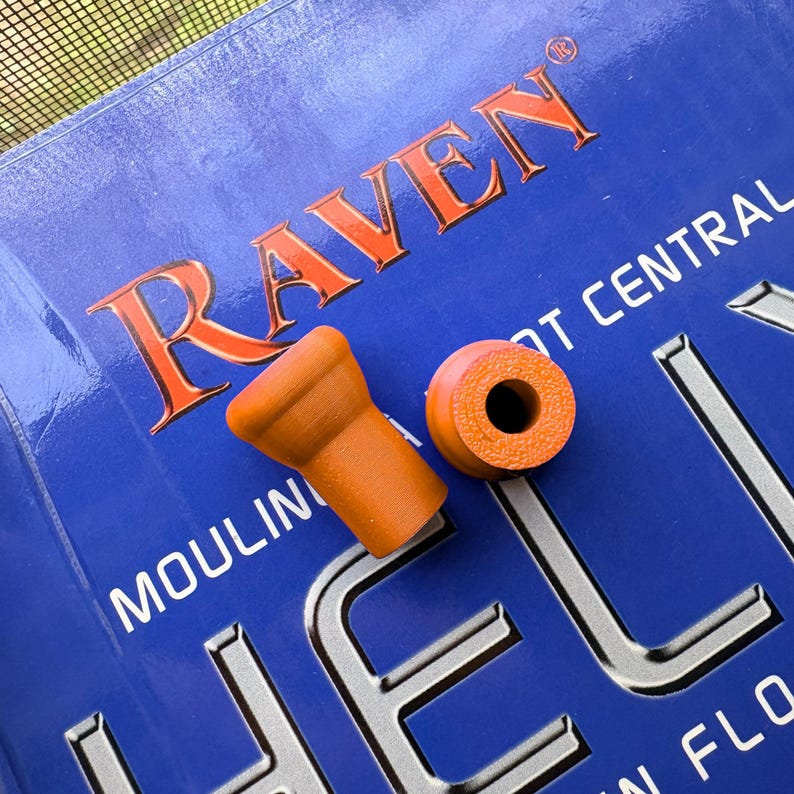 K&ouml;nnte beinhalten: Zwei orangefarbene Gummiteile auf einer blauen Oberfl&auml;che mit dem Wort "RAVEN" in Orange. Ein Teil ist zylindrisch, das andere hat eine kleine, ausgestellte Form. Der Hintergrund ist eine blaue Oberfl&auml;che mit wei&szlig;em Text.