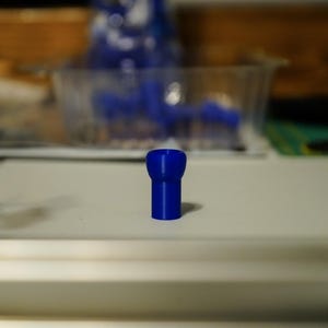 K&ouml;nnte beinhalten: Ein kleiner, leuchtend blauer Kunststoffgegenstand mit zylindrischem Sockel und breiterem Oberteil. Der Gegenstand steht auf einer wei&szlig;en Oberfl&auml;che. Weitere blaue Objekte sind im Hintergrund zu sehen.