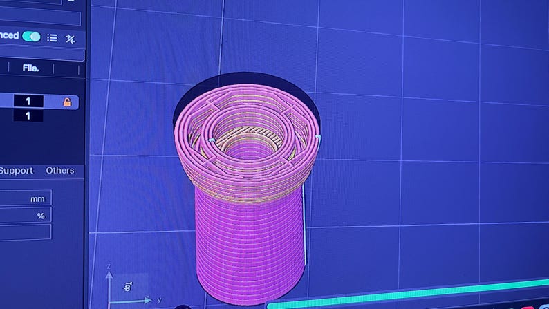 K&ouml;nnte beinhalten: Ein 3D-gerendertes Modell eines zylindrischen Objekts mit einem komplexen, geschichteten Design. Das Objekt ist haupts&auml;chlich rosa mit gelben und beigen Akzenten und vor einem blauen Rasterhintergrund platziert. Es ist ein digitales Rendering.