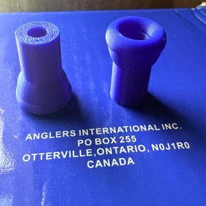 May include: Two purple, 3D-printed nozzles. One is cylindrical with a flared base, the other is a flared cone shape. The nozzles are on a blue surface with white text that reads: ANGLERS INTERNATIONAL INC. PO BOX 255 OTTERVILLE, ONTARIO, N0J1R0 CANADA.