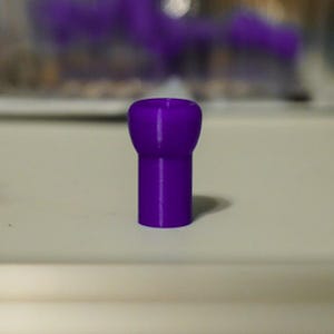 K&ouml;nnte beinhalten: Ein massives lila Objekt mit abgerundeter Oberseite und zylindrischem Sockel. Das Objekt hat einen leuchtenden Lilaton und scheint aus einem glatten Material zu bestehen. Das Objekt steht auf einer wei&szlig;en Oberfl&auml;che.