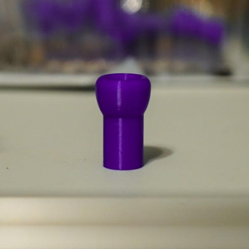 K&ouml;nnte beinhalten: Ein massives lila Objekt mit abgerundeter Oberseite und zylindrischem Sockel. Das Objekt hat einen leuchtenden Lilaton und scheint aus einem glatten Material zu bestehen. Das Objekt steht auf einer wei&szlig;en Oberfl&auml;che.