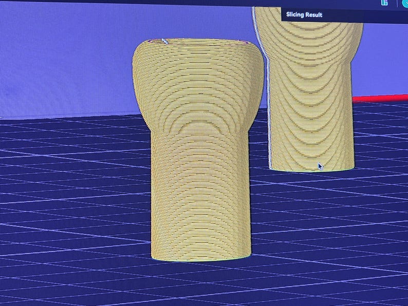 K&ouml;nnte beinhalten: Zwei gelbe, zylindrische Objekte mit abgerundeten Oberteilen werden vor einem blauen Gitterhintergrund dargestellt. Die Objekte scheinen 3D-Modelle oder Prototypen zu sein, m&ouml;glicherweise f&uuml;r ein Designprojekt. Der Text "Slicing Result" ist oben im Bild zu sehen.