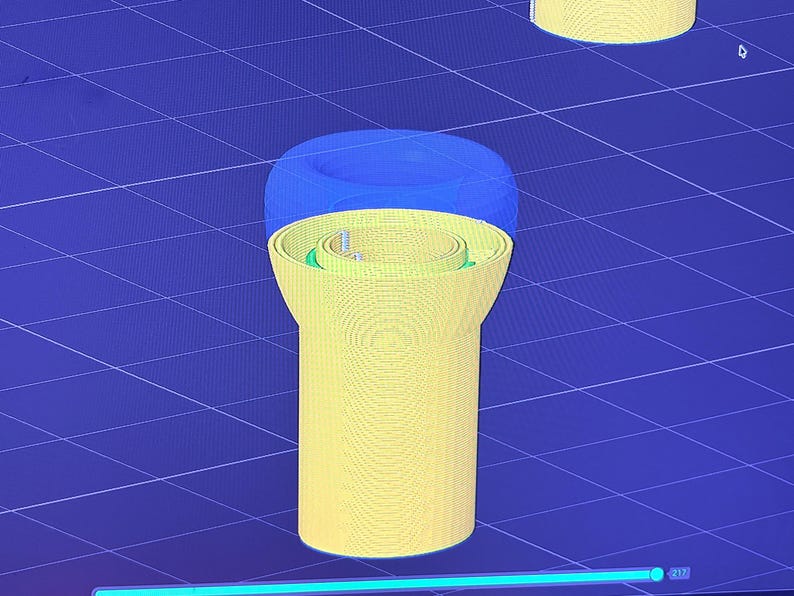 K&ouml;nnte beinhalten: Ein 3D-Rendering eines gelben zylindrischen Objekts mit blauem Deckel. Das Objekt hat ein detailliertes Inneres mit gr&uuml;nen und silbernen Akzenten. Der Hintergrund ist ein blaues Gittermuster.