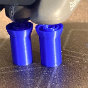 K&ouml;nnte beinhalten: Zwei leuchtend blaue, zylindrische Objekte mit einem ausgestellten oberen Teil werden von einem 3D-Drucker erstellt. Der Druckkopf ist &uuml;ber den Objekten sichtbar. Der Text "CAUTION HOT" ist auf dem Drucker aufgedruckt.