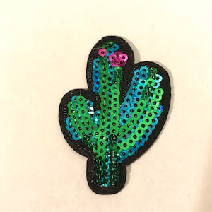 May include: A green and blue sequined cactus patch with a pink flower on top. The patch is on a white background.