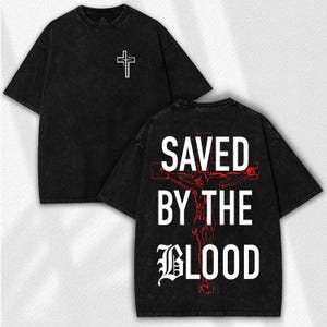 May include: Black t-shirt with a white cross on the front and the text "SAVED BY THE BLOOD" with a red cross and Jesus graphic on the back. The shirt has a washed, vintage look.