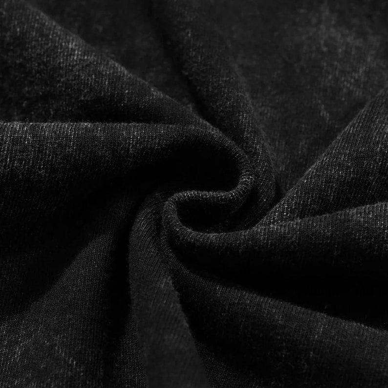 May include: Close-up of black fabric with visible texture and folds. The material appears to be a dark, solid color, with subtle variations in tone. The fabric is tightly woven, and the image highlights the texture and depth of the material.