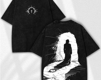 May include: Black t-shirt with a white graphic of a cross surrounded by a sunburst design on the front. The back features a black and white illustration of a person walking towards a bright light.
