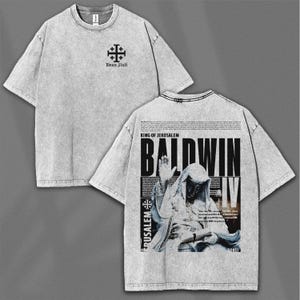 May include: A light grey t-shirt with a faded, textured appearance. The front features a black cross design and text. The back displays a graphic of King Baldwin IV with the text "King of Jerusalem" and "Baldwin IV".