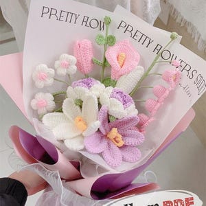 Könnte beinhalten: Ein handgefertigter Häkelblumenstrauß in Rosa, Weiß und Lila, verpackt in rosa und lila Papier. Der Strauß enthält verschiedene Blumenarten mit grünen Stielen und Blättern. Der Text "PRETTY FLOWERS" ist auf der Verpackung zu sehen.