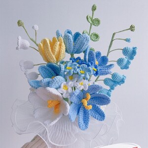 Könnte beinhalten: Ein handgefertigter Blumenstrauß aus Häkelfäden in Blau-, Weiß- und Gelbtönen. Der Strauß enthält Tulpen, Gänseblümchen und andere florale Designs mit grünen Stielen und Blättern. Der Strauß wird in einem weißen, gerüschten Kragen gehalten. Der Text "Pattern PDF" ist sichtbar.