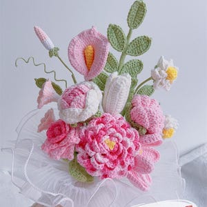 Könnte beinhalten: Ein handgefertigter Häkelblumenstrauß mit Rosen, Calla-Lilien und anderen Blumen in Rosa-, Weiß- und Grüntönen. Der Strauß wird von einem weißen, gerüschten Kragen zusammengehalten. Der Text "Pattern PDF" ist sichtbar.