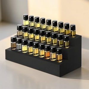 May include: A tiered black display holding numerous small glass bottles with black caps. The bottles contain various shades of amber and clear liquids, arranged neatly on the stepped platform. The setup suggests a fragrance or essential oil collection.