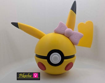 May include: A yellow and black Pikachu-themed decorative item with a pink bow. The item has red circles on the bottom and black accents. The text "Pikachu" is displayed on a black rectangle with a female symbol.