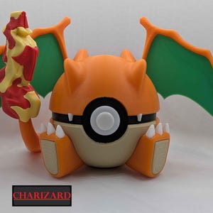 May include: A 3D-printed Charizard figure in a Poké Ball design. The figure is primarily orange with green wings and white claws. A flame is attached to the figure. The word "CHARIZARD" is printed on a black rectangle.