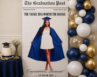 May include: A graduation party scene featuring a large newspaper-style sign with the headline "The Graduation Post" and the text "The Tassel Was Worth The Hassle." A graduate in a blue gown and white dress is featured. Balloons in gold, white, and navy blue decorate the scene.