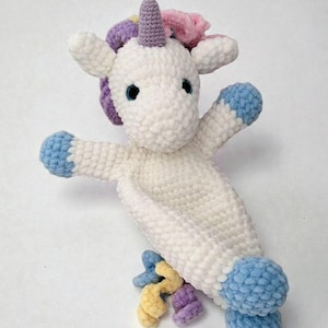 May include: A white crocheted unicorn plush toy with blue hooves and accents. The unicorn has a purple horn, blue eyes, and a colorful mane of pink, purple, and yellow. The toy is soft and cuddly.
