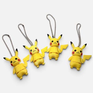 May include: Four yellow Pikachu character keychains, each featuring a small metal ball chain loop attached to the top of the head. The figures have pointed ears with black tips, red circular cheeks, and a lightning bolt-shaped tail on the side.