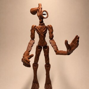 Puede incluir: Figura de acci&oacute;n de Siren Head marr&oacute;n con articulaciones. La figura tiene una cabeza en forma de sirena con una boca con dientes blancos. Los brazos de la figura est&aacute;n extendidos y las piernas est&aacute;n de pie. La figura es de pl&aacute;stico.